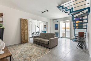 Uma sala de estar com sofá, tapete estampado, máquina de costura antiga e escada espiral azul.