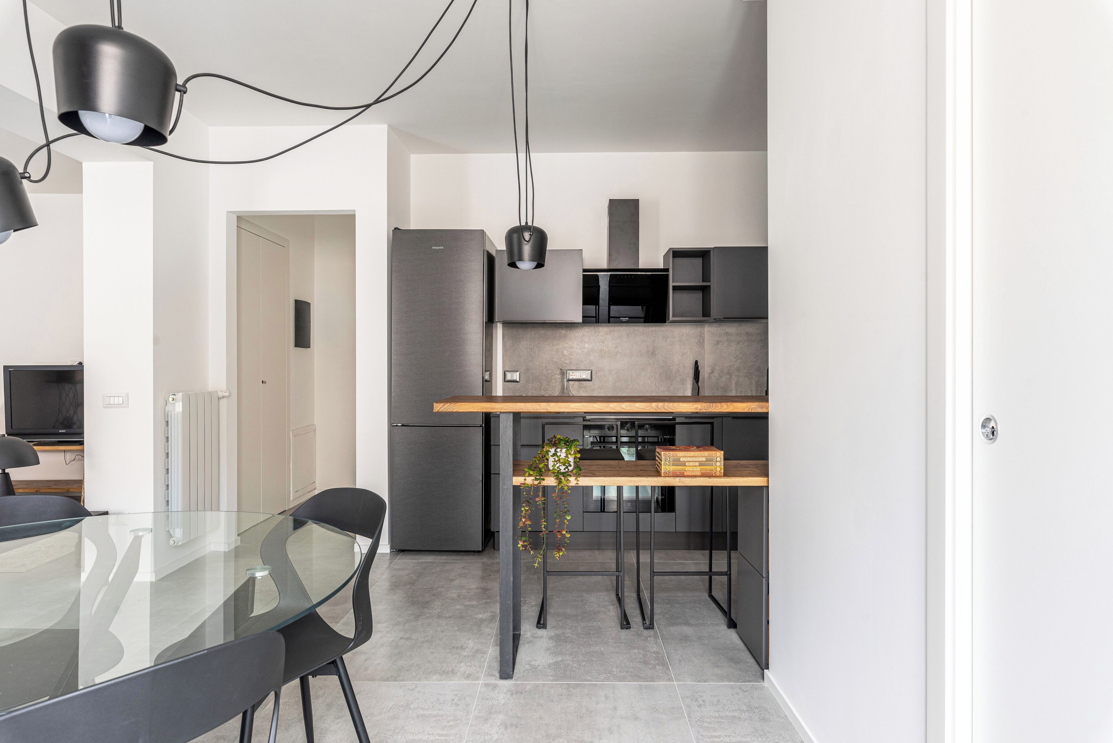 A modern kitchen with a glass dining table, black chairs, and pendant lighting.