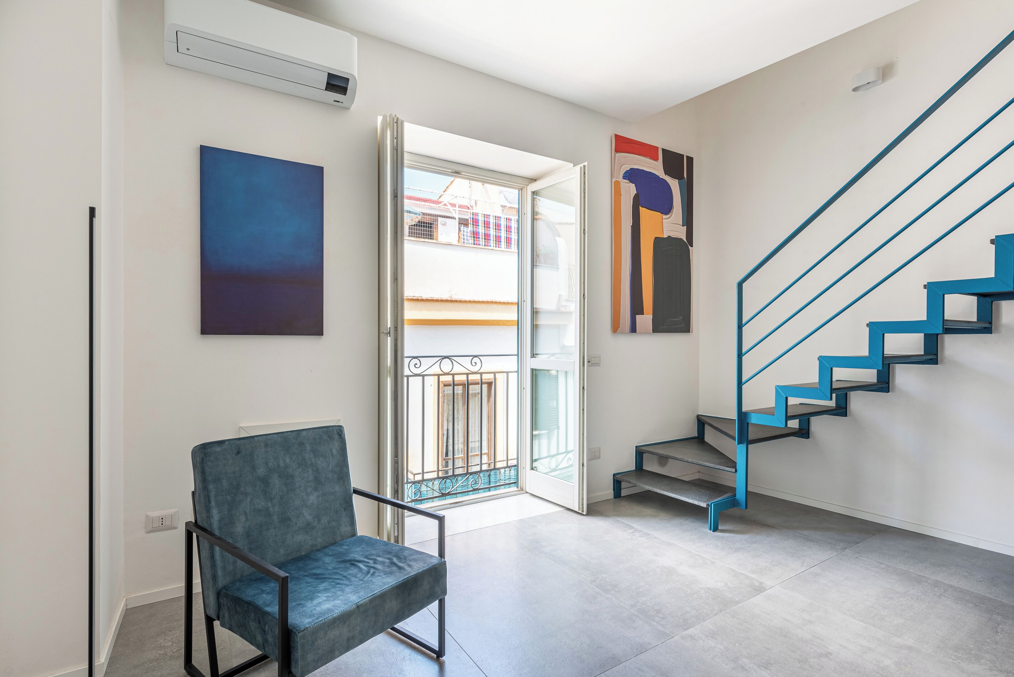 A modern interior with a blue chair, a staircase with blue railings, and a door leading outside.