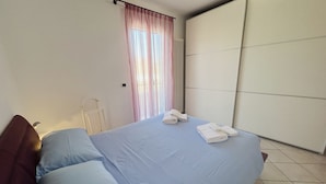Camera da letto con un letto, cuscini, termosifone, finestra con tende e un armadio.