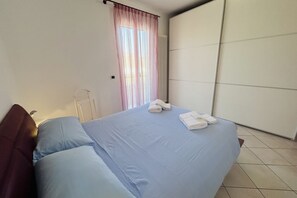 Un dormitori amb llit, almoines, un radiador, una finestra amb cortines i un armari.