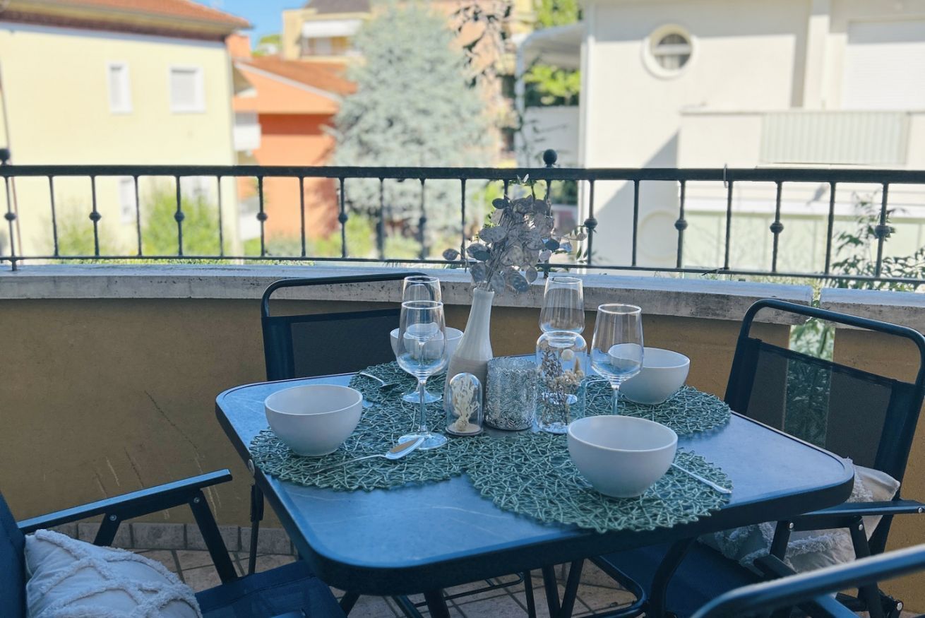A balcony with a table set for dining, chairs, and a railing.