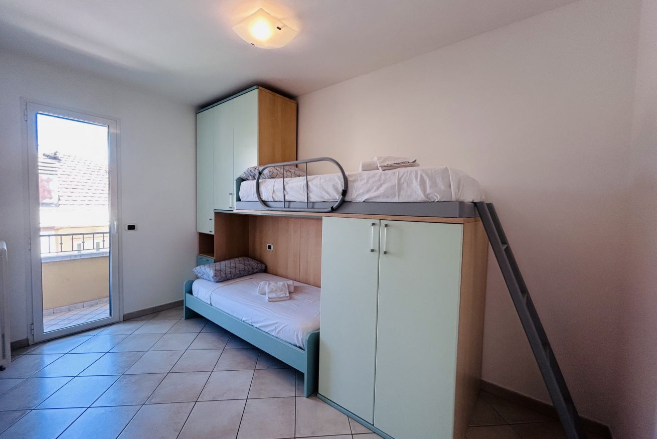 A dorm-style room with a bunk bed, a wardrobe, and a sliding door leading to a balcony.