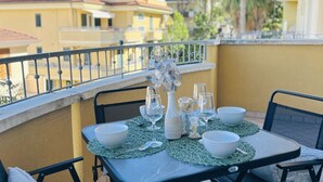 A balcony with a table set for four, a vase with flowers, and a view of buildings and trees. - Viktor Flexrent - Abyssinia Real Estate (Riccione)