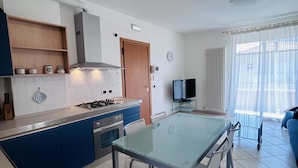 Una cucina moderna con piano cottura a gas, forno e pensili blu. C'è un tavolo da pranzo con sedie e una TV nella zona living.