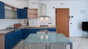 Una cucina moderna con mobili blu, un tavolo da pranzo in vetro e una porta in legno.