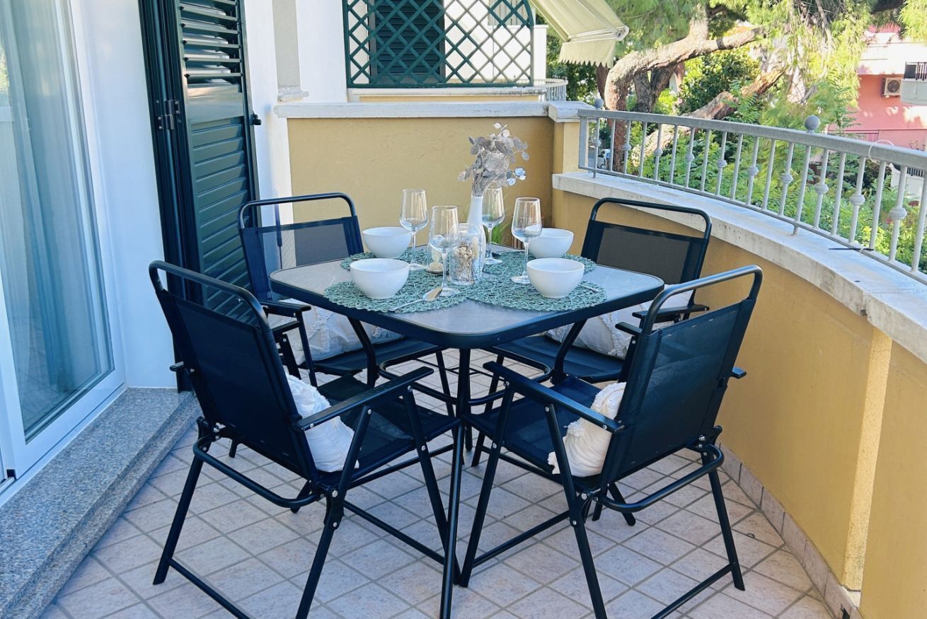 A balcony with a table set for four, chairs, and a vase with flowers.