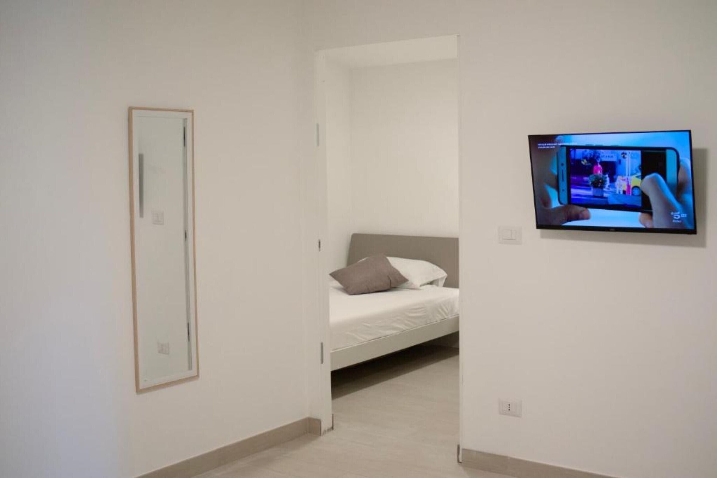 A bedroom with a bed, a TV mounted on the wall, and a door leading to another room.