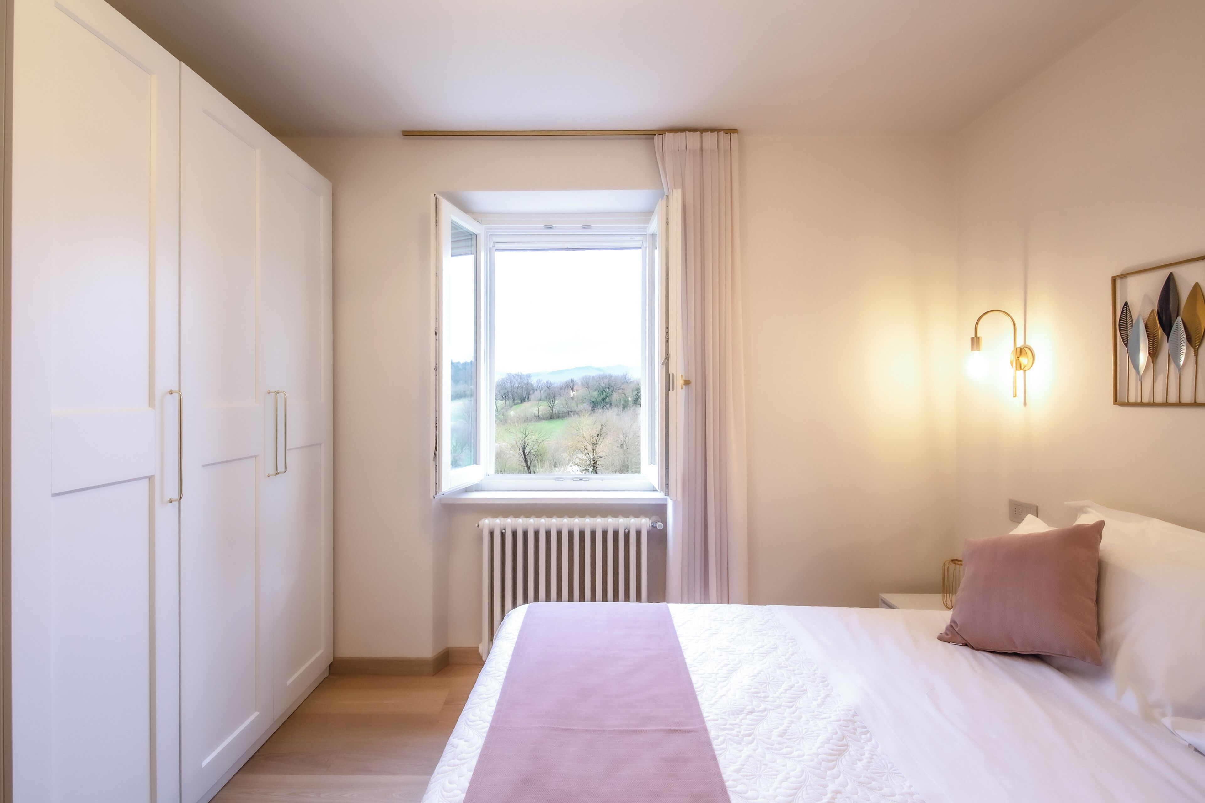 Una camera da letto con un letto, una finestra vista, un termosifone e una lampada a parete.