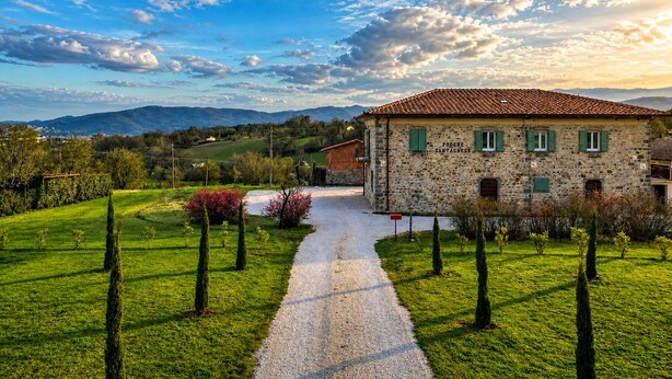 A stone building with a tiled roof, a gravel path, and a green landscape with trees. - Modern and refined country house (Bibbiena)