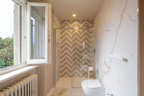 A bathroom with a shower, toilet, and a window with an open shutter.