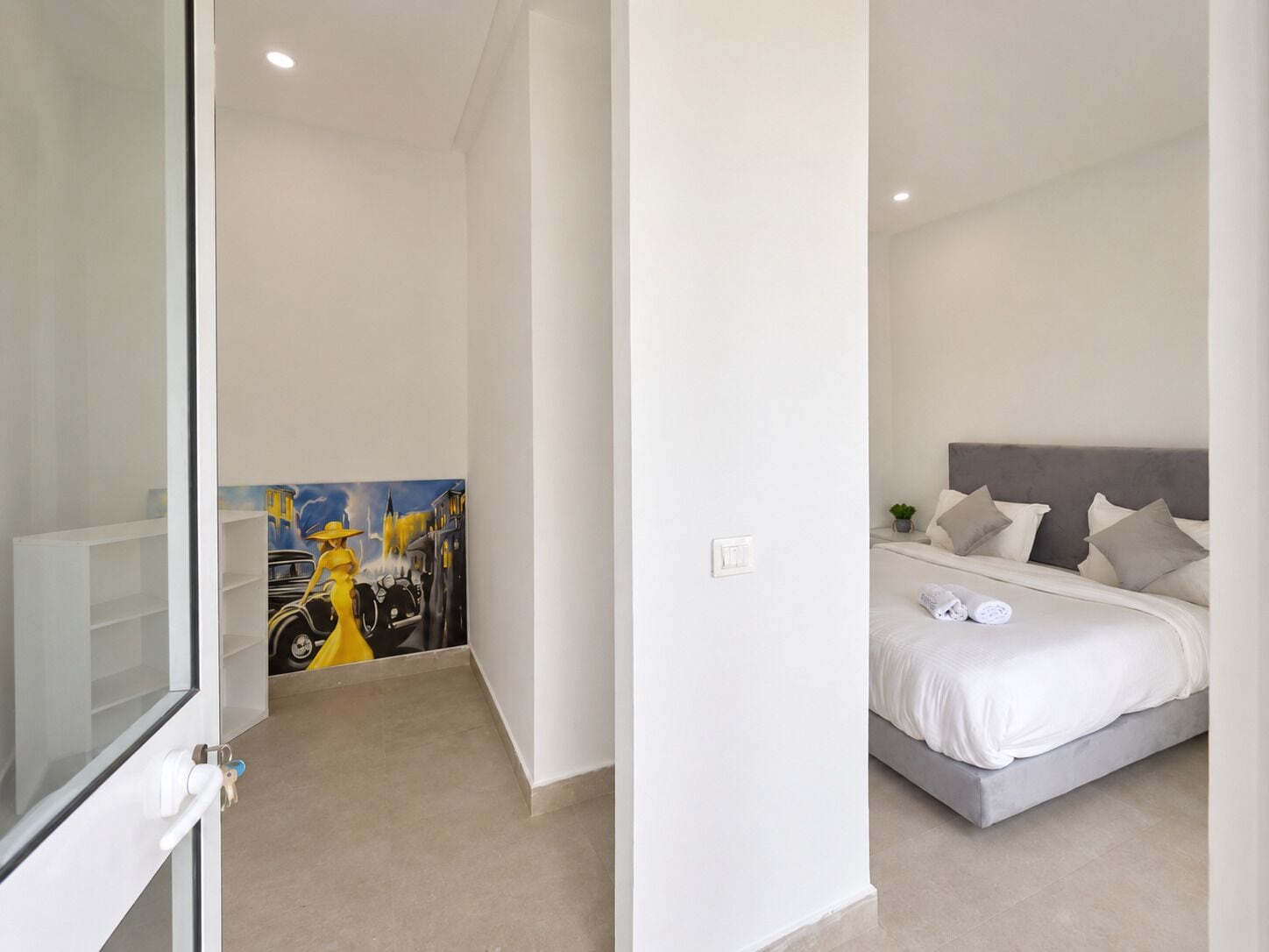 Ein Schlafzimmer mit einem Bett, Kissen, einer kleinen Pflanze und einem Bild an der Wand.