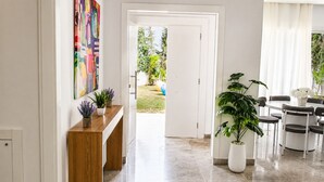 A hallway with a wooden bench, potted plants, a door leading to a garden, and a dining area with chairs and a table. - Elegant Villa in Gammarth With Private Indoor Pool (La Marsa)