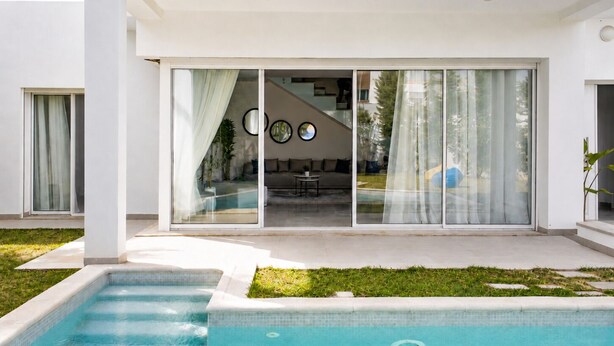 A modern house with a swimming pool, large sliding glass doors, and a patio area. - Elegant Villa in Gammarth With Private Indoor Pool (La Marsa)