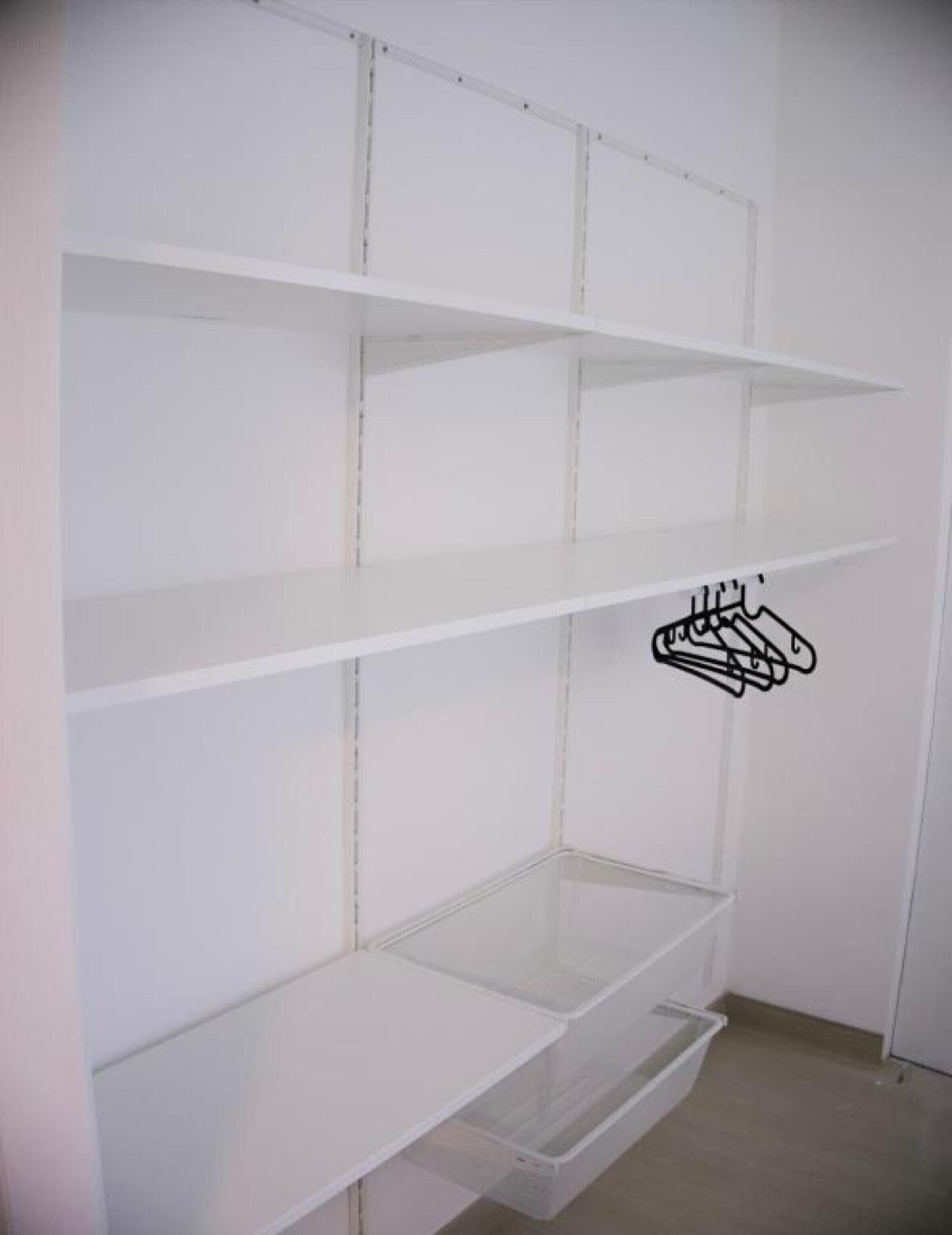 Un coin de pièce aux murs blancs, avec une étagère blanche à trois niveaux et un tiroir inférieur.