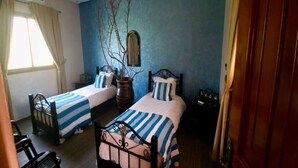 A bedroom with two beds, a potted plant, a mirror, and a window with curtains. - ferme les oliviers palais d'hôtes (Sidi Abdallah Ghiat)