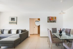 Een moderne woonkamer met een bank, voetenbankje, eettafel, stoelen en kunstwerken aan de muur.