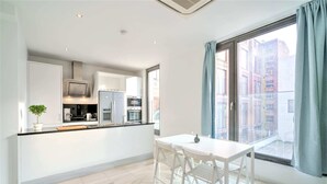 A modern kitchen with white cabinetry, a dining table with chairs, and a large window with curtains. - 1-bedroom Lodge Stay in Antwerp (Antwerp)