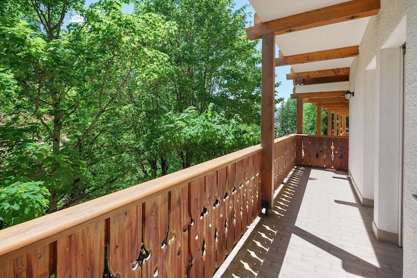 A wooden balcony with a view of green trees. - Apartment 'Lella Genziana' with Mountain View, Balcony and Wi-Fi (Vigo di Fassa)