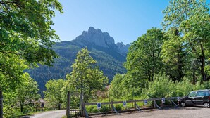 A gravel road leading to a gated parking area with a mountain in the background. - Apartment 'Lella Genziana' with Mountain View, Balcony and Wi-Fi (Vigo di Fassa)