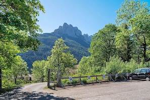A gravel road leading to a gated parking area with a mountain in the background. - Apartment 'Lella Genziana' with Mountain View, Balcony and Wi-Fi (Vigo di Fassa)