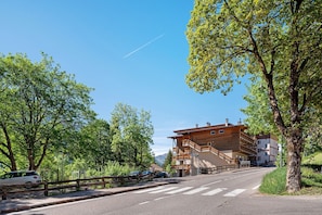 A road leading to a multi-story building with balconies, surrounded by trees and a clear sky. - Apartment 'Lella Genziana' with Mountain View, Balcony and Wi-Fi (Vigo di Fassa)