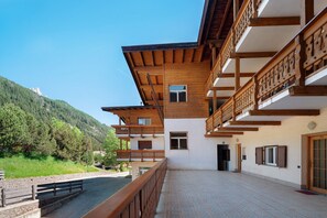 Ein mehrstöckiges Gebäude mit Balkonen, einer gepflasterten Terrasse und einer Bergkulisse.