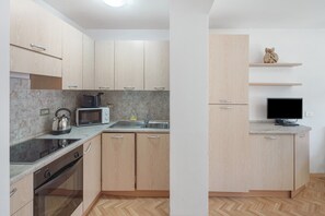 Eine moderne Küche mit Herd, Mikrowelle und Spüle. Ein Fernseher steht auf einem Schrank und ein Regal zeigt eine Dekoration.