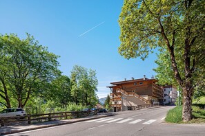 Eine Straße führt zu einem mehrstöckigen Gebäude mit Balkonen, umgeben von Bäumen und einem klaren Himmel.