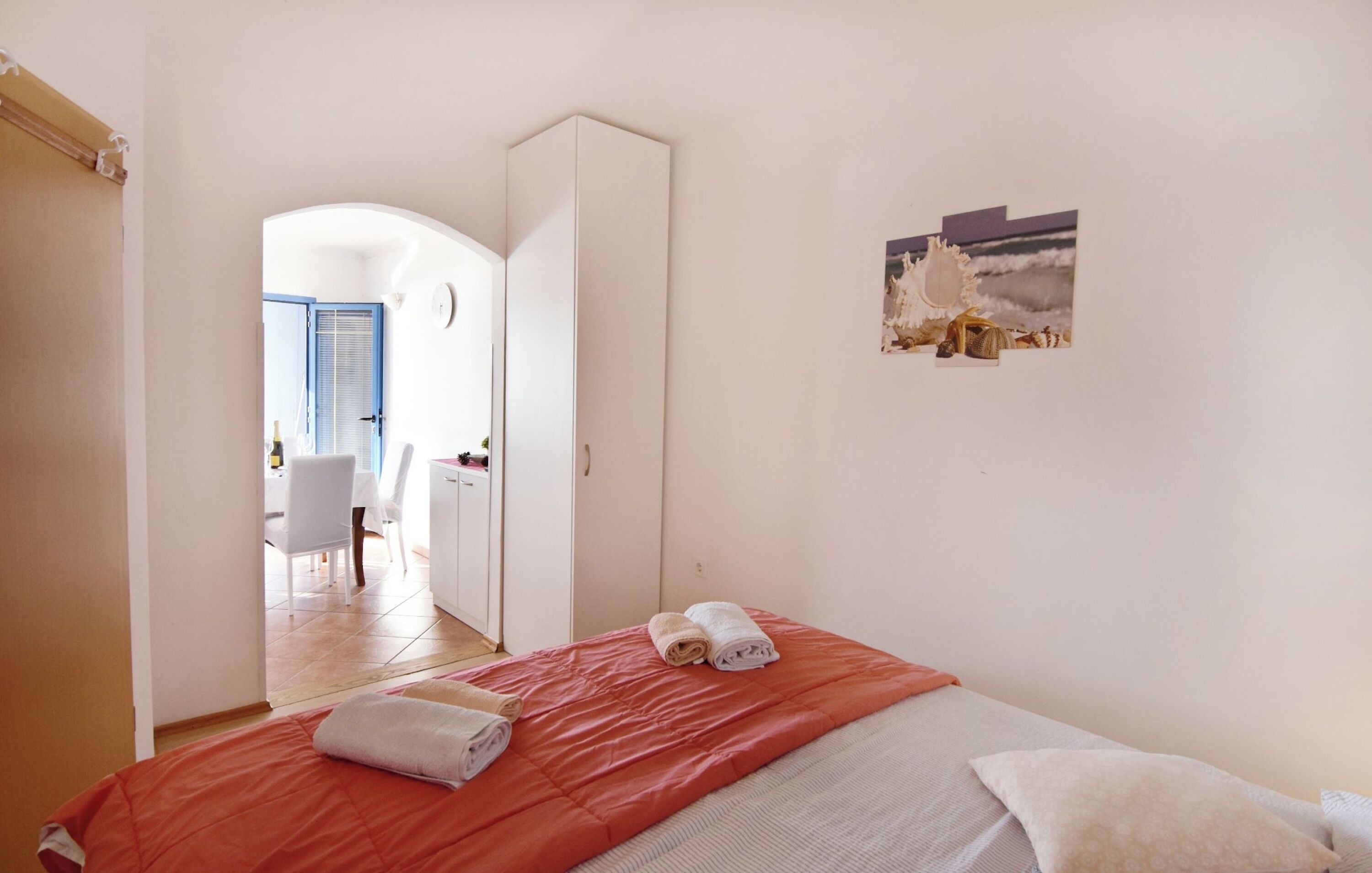 Un dormitorio con cama, un armario blanco, una mesita con silla y un cuadro en la pared.