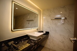 Un bany amb un mirall gran, un lavabo blanc, parets de marbre i una superfície de taulell negra.
