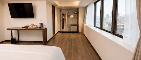 A hotel room with a bed, a desk, a TV, an air conditioning unit, a window with a city view, and a walk-in closet.
