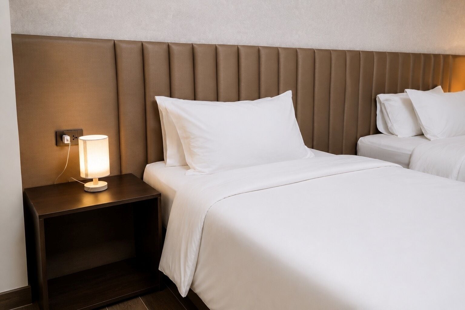 A hotel room with a bed, a bedside table with a lamp, and a headboard.