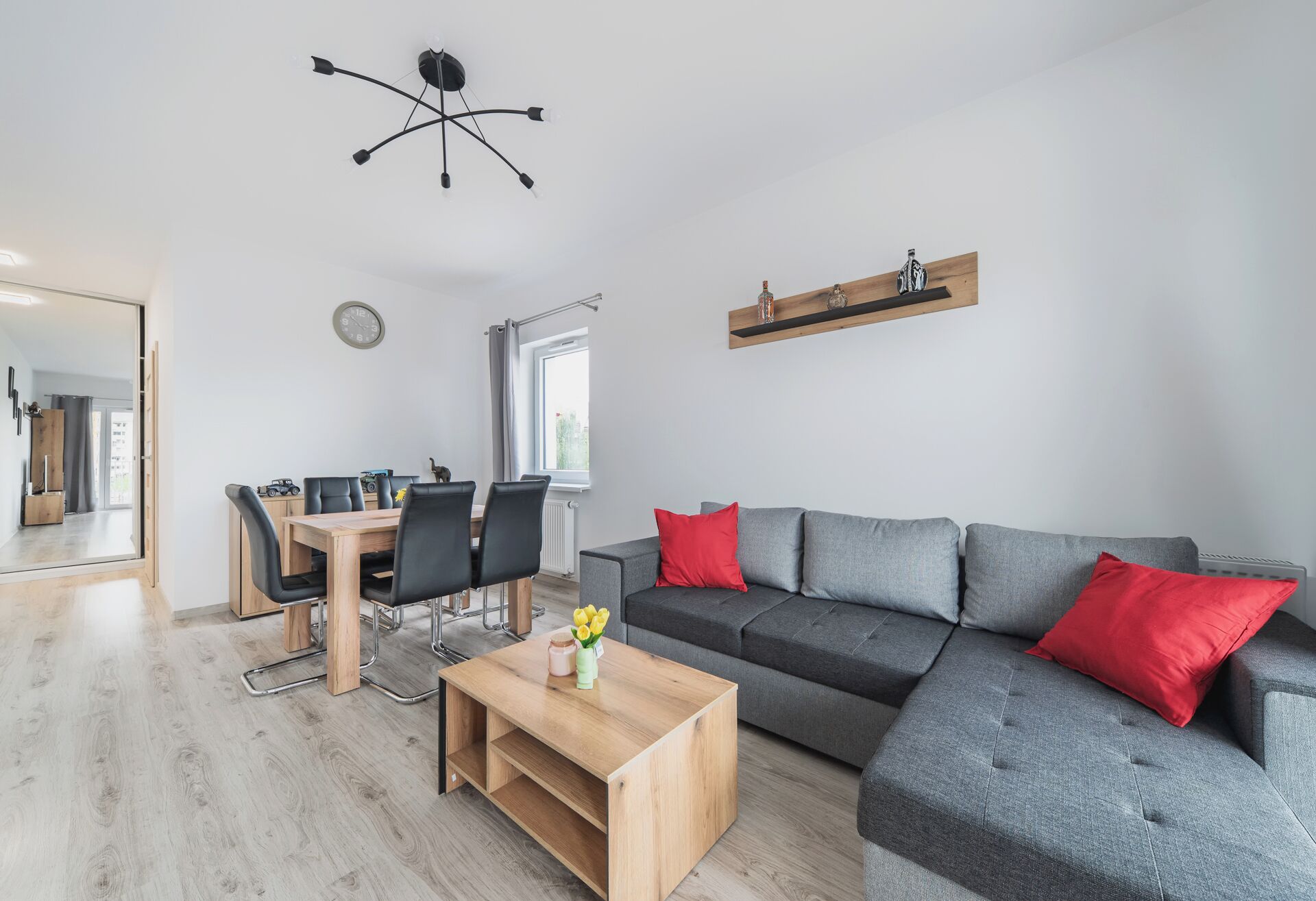 A modern living room with a dining area, grey sofa, wooden coffee table, and a ceiling light fixture.