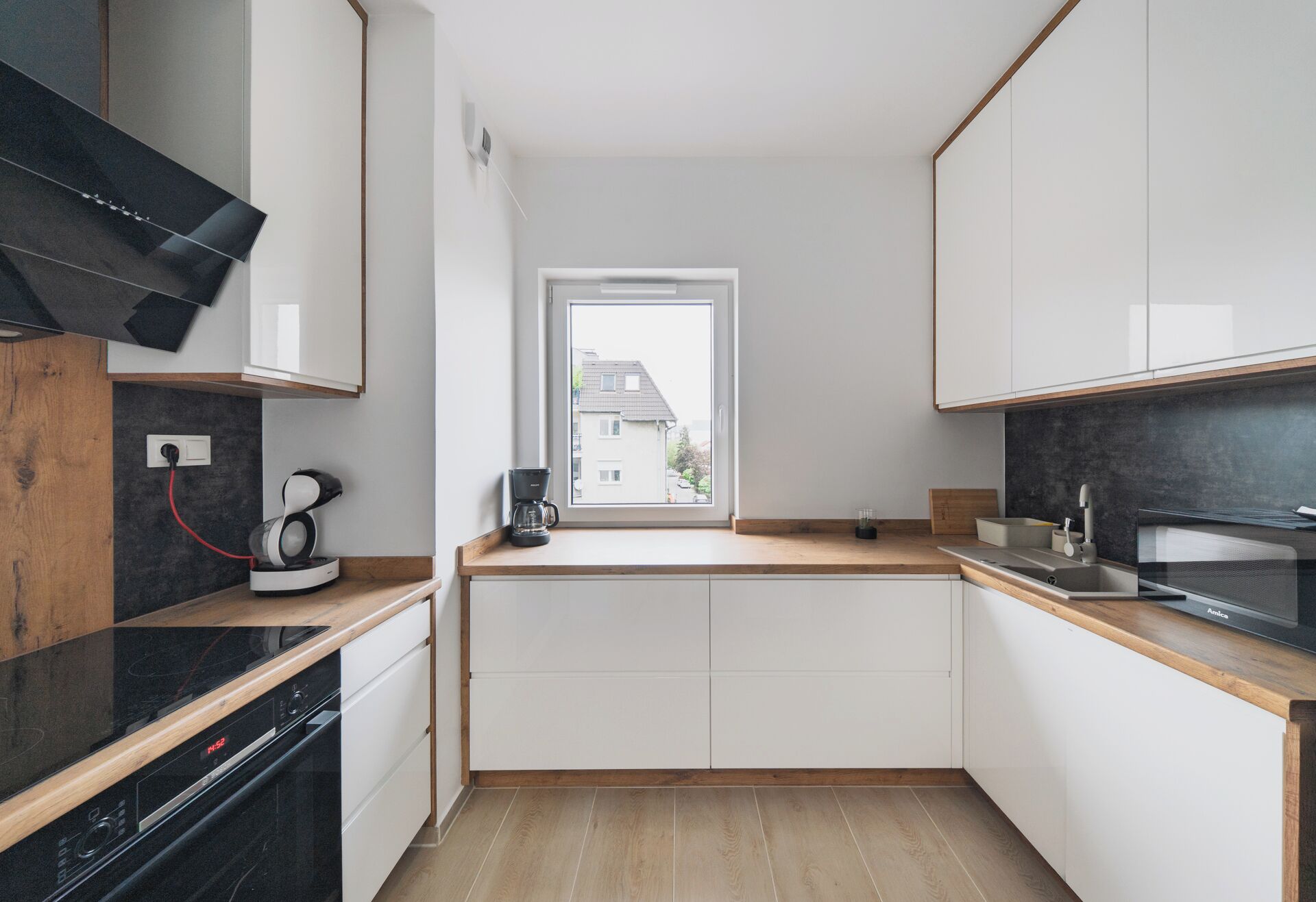 A modern kitchen with white cabinets, a black countertop, and a window with a view of a house.