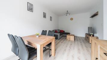 Ein modernes Wohnzimmer mit Essbereich, einer Couch, einem Fernseher und einer Kristallleuchtre.