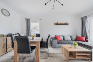Ein modernes Wohnzimmer mit Essbereich, grauem Sofa, Holztisch und Blick auf die Stadt.