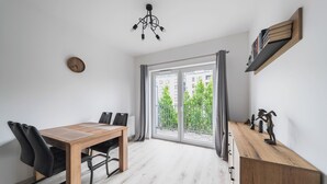 Habitación moderna con mesa de comedor de madera, sillas negras, lámpara de techo, puerta corrediza de vidrio con vista a la vegetación y un pequeño armario de madera con objetos decorativos.