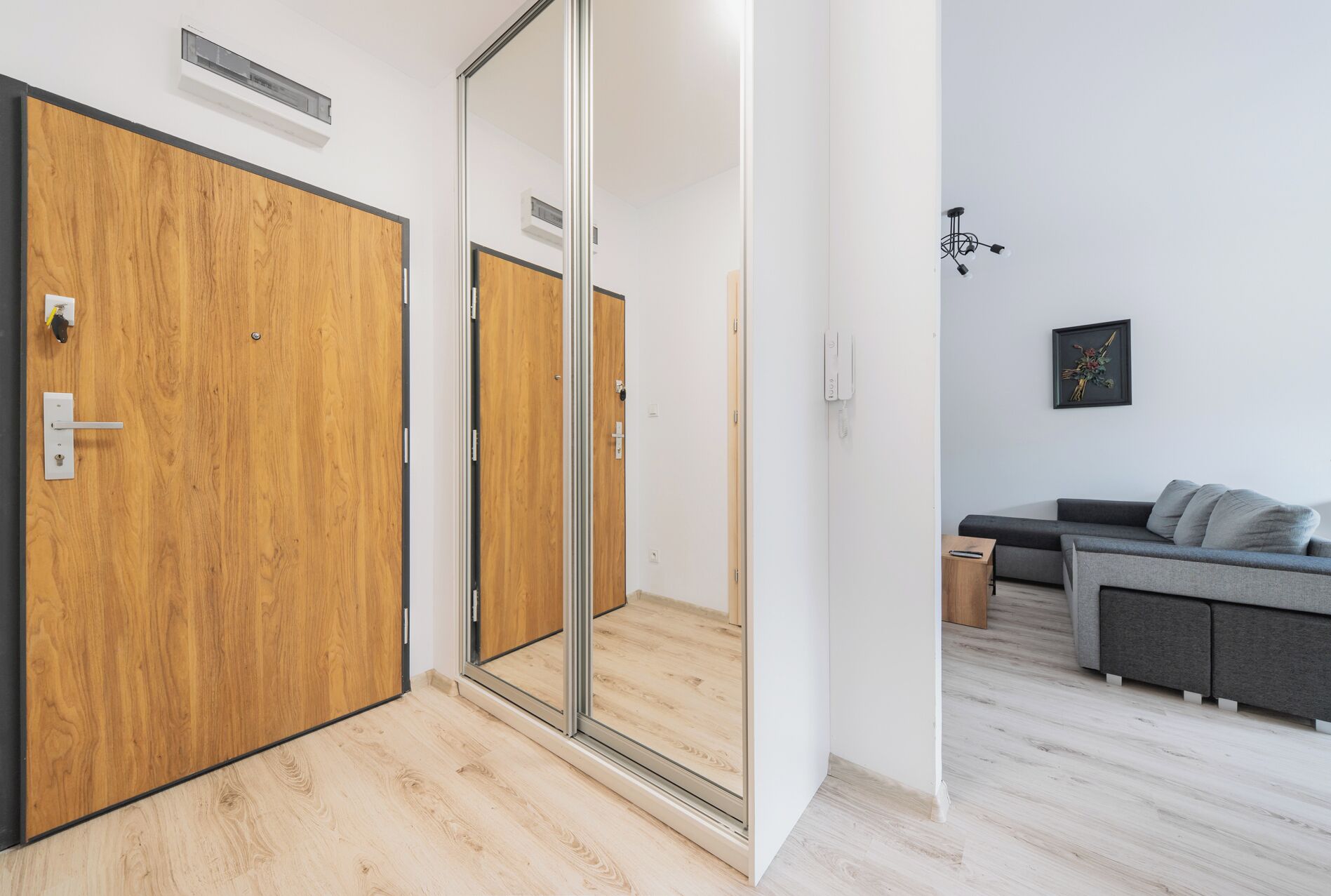Una camera moderna con una porta in legno, una porta scorrevole in vetro, un divano grigio e un tavolino.