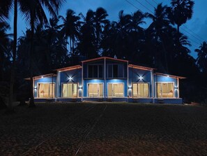 A two-story building with large windows and a flat roof, surrounded by palm trees. - Aarambh The Creek Breeze Resort (Palghar)