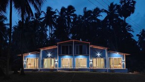 A two-story building with large windows and a flat roof, surrounded by palm trees. - Aarambh The Creek Breeze Resort (Palghar)