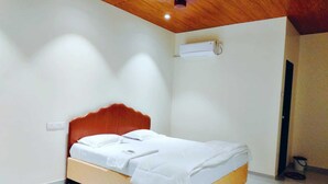 A bedroom with a wooden headboard, white bedding, a ceiling fan, and an air conditioning unit. - Aarambh The Creek Breeze Resort (Palghar)