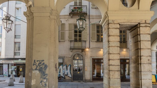 An urban street scene with a building facade, a door with graffiti, and a hanging lantern. - Conte Verde - Bilo 7 Grey by Wonderful Italy (Turin)