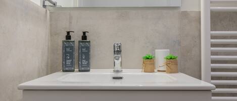A bathroom with a white sink, two soap dispensers, a faucet, and two small potted plants.