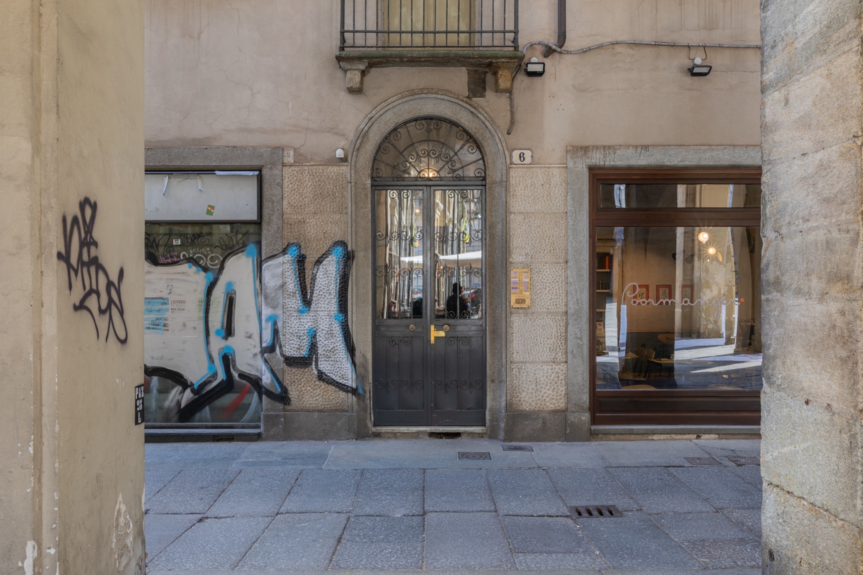 A building facade with a black metal door, a window with graffiti, and a visible number '6' on the wall.