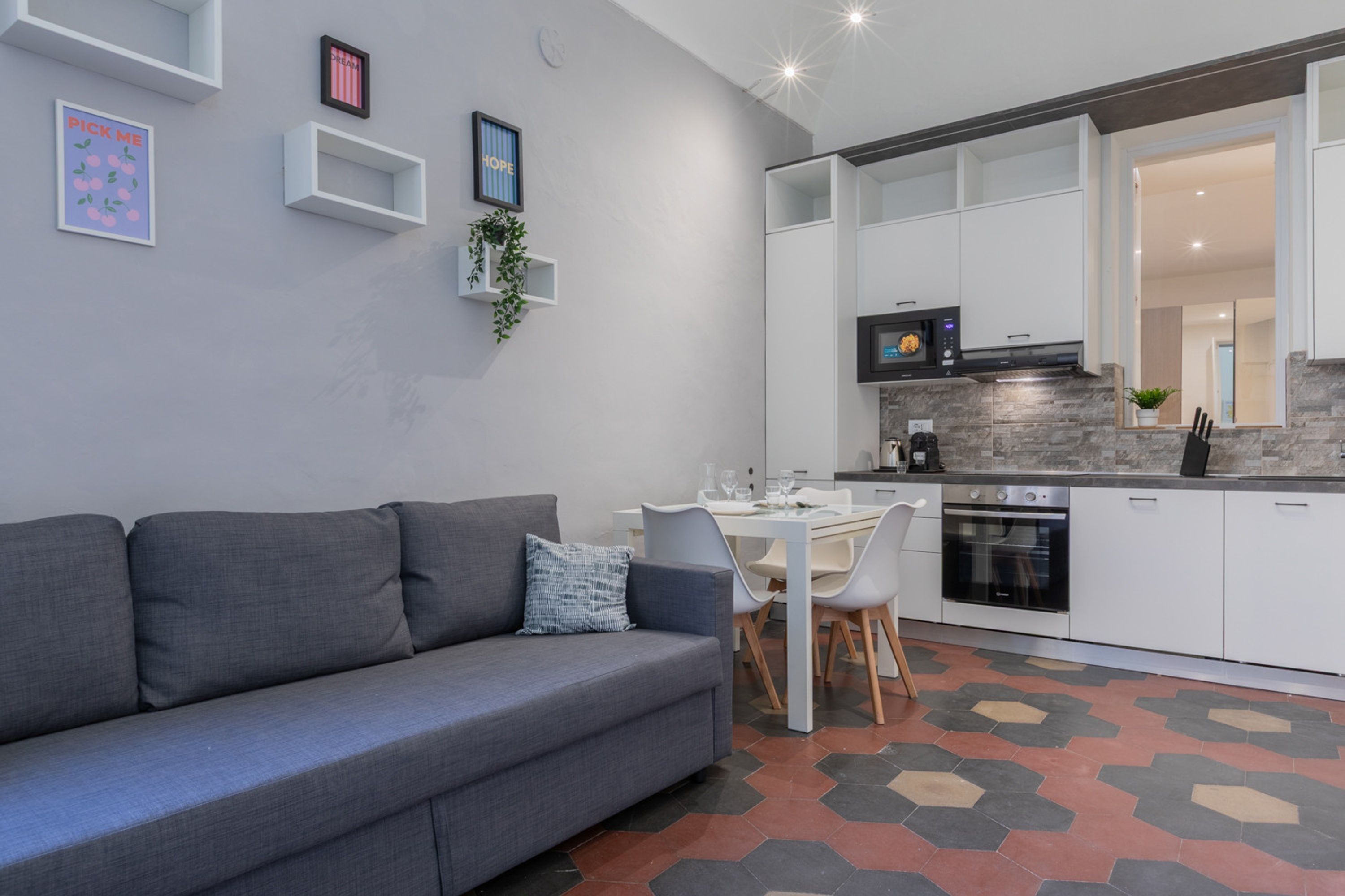Een moderne woonkamer met een grijze bank, een eettafel met stoelen, en een keuken met witte kasten en een inbouwoven.