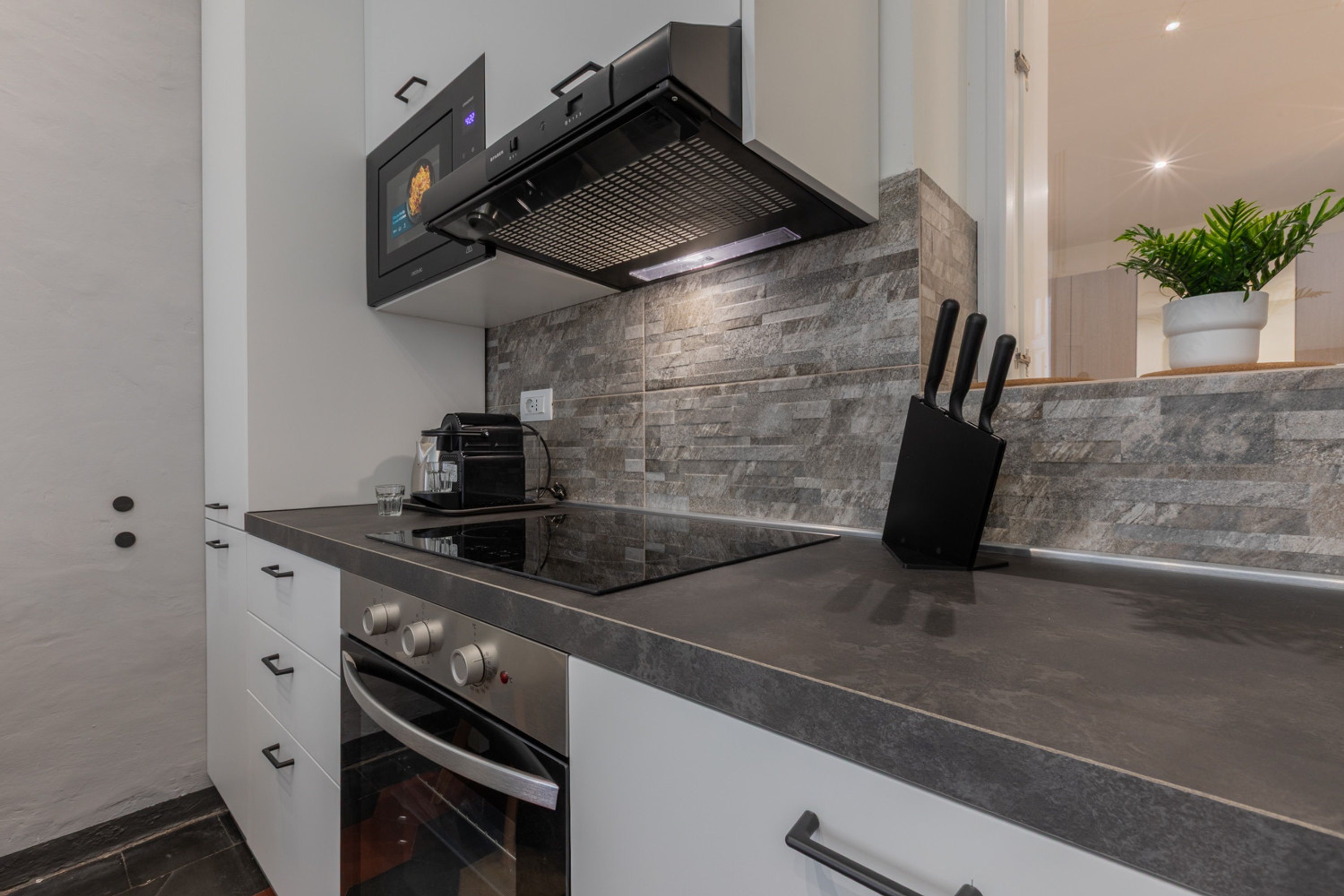 Una cocina moderna con horno empotrado, estufa, microondas y campana extractora negra.