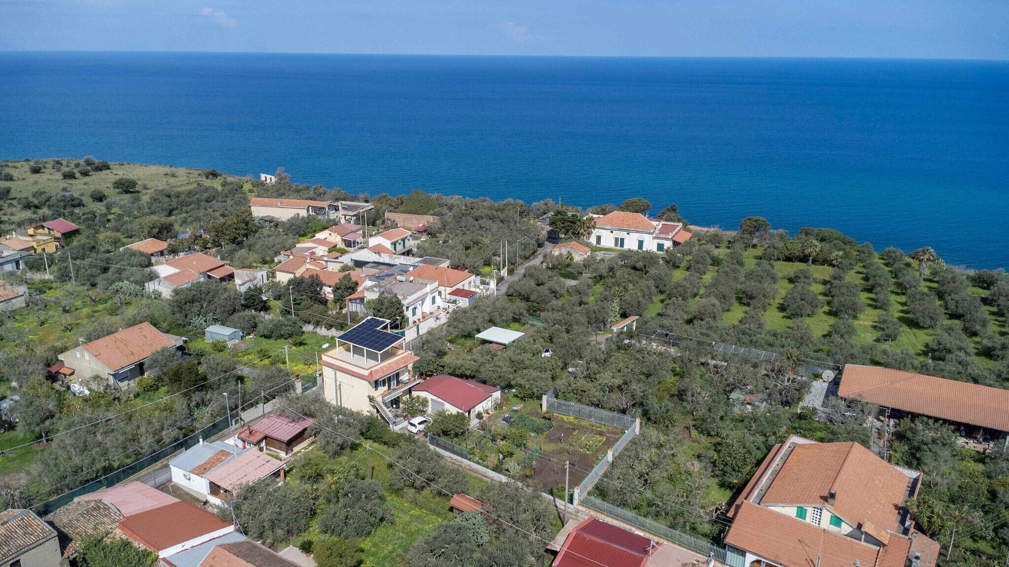 Vista aerea di una zona residenziale costiera con case, un edificio bianco ben visibile e vista sul mare.