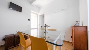 A dining area with a glass table, yellow chairs, a wooden cabinet, and a flat-screen TV mounted on the wall. - Apartment 'Vanedda di Mari - Casa Nespolo' with Shared Terrace, Wi-Fi and Air Conditioning (Messina)