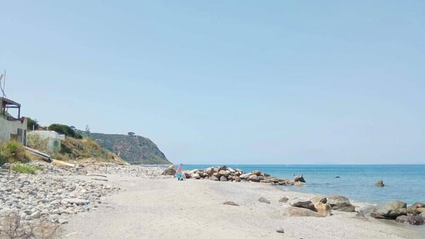 A beach with a rocky shoreline, a person walking, and a building on the left. - Apartment 'Vanedda di Mari - Casa Nespolo' with Shared Terrace, Wi-Fi and Air Conditioning (Messina)